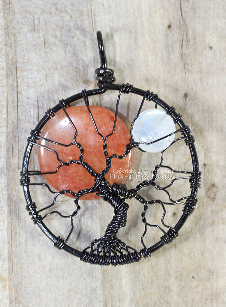 Large, orange opal sun and small rainbow moonstone moon rest together in this black wire wrapped tree of life pendant by PhoenixFire Designs.